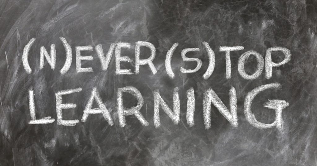 Photo of a Blackboard with writing in chalk: Never Stop Learning or Ever Top Learning