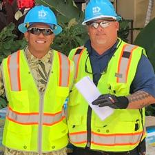 Two men in construction vests and hard hats smiling